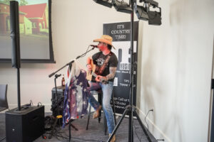 A musician donning a cowboy hat performs at a graduation party, providing live entertainment in a venue suitable for a graduation celebration, complete with professional audio equipment and a custom backdrop to enhance the festive atmosphere