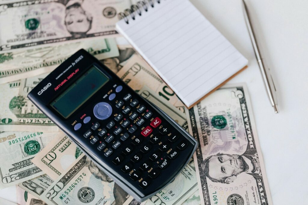 Casio calculator on top of us dollar bills with a notepad and pen, depicting financial planning or budgeting - ideal for articles about managing expenses for events such as graduation parties.