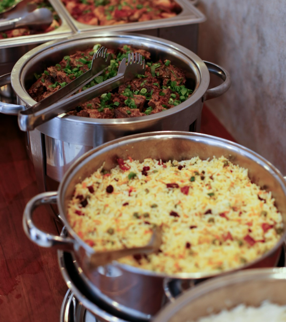 Assorted catering dishes with savory meats and seasoned rice in stainless steel chafing dishes, ready to be served at a graduation party banquet.