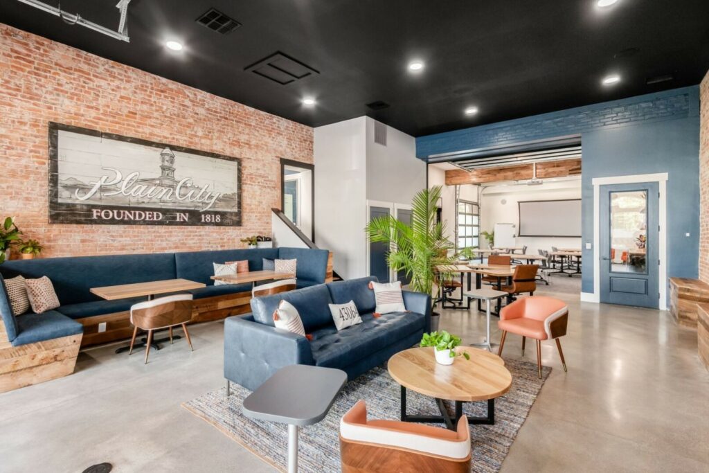 Spacious and modern graduation party venue with exposed brick walls and a large 'plain city' sign, featuring comfortable blue and tan seating areas perfect for hosting a stylish and memorable event.