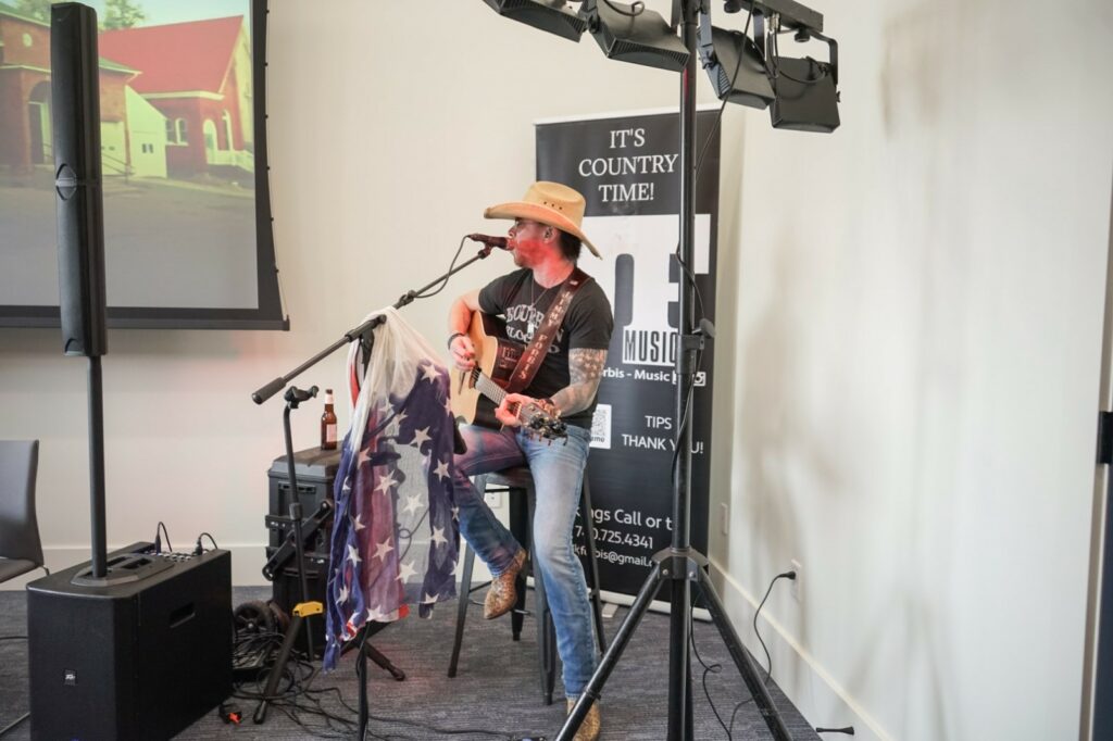 Live country music performer playing guitar at a graduation party, adding a touch of americana with a cowboy hat and an american flag-themed chair, ready to entertain the guests