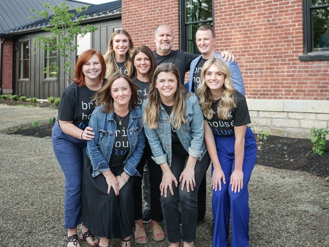 Smiling team of event staff ready to assist with a graduation party, standing in front of the 'brick house blue' venue, showcasing their teamwork and hospitality.