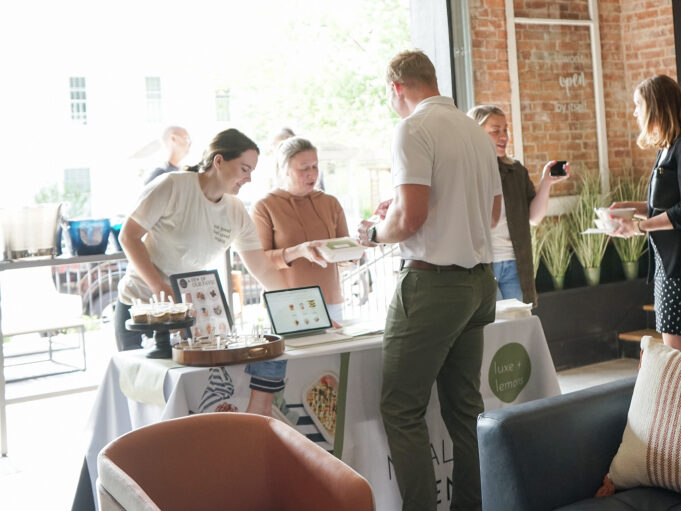 Event attendees engaging with vendors at an expo in a graduation party venue with an industrial chic ambiance, highlighted by an open garage door and brick walls