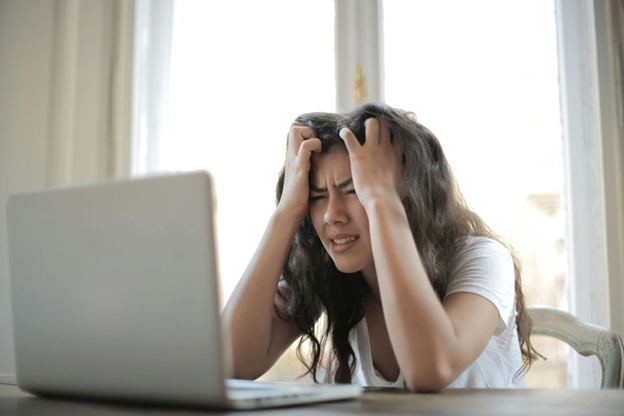 Young woman experiencing stress while working on her laptop at home, showcasing the challenges of remote work and the need for effective work-life balance solutions