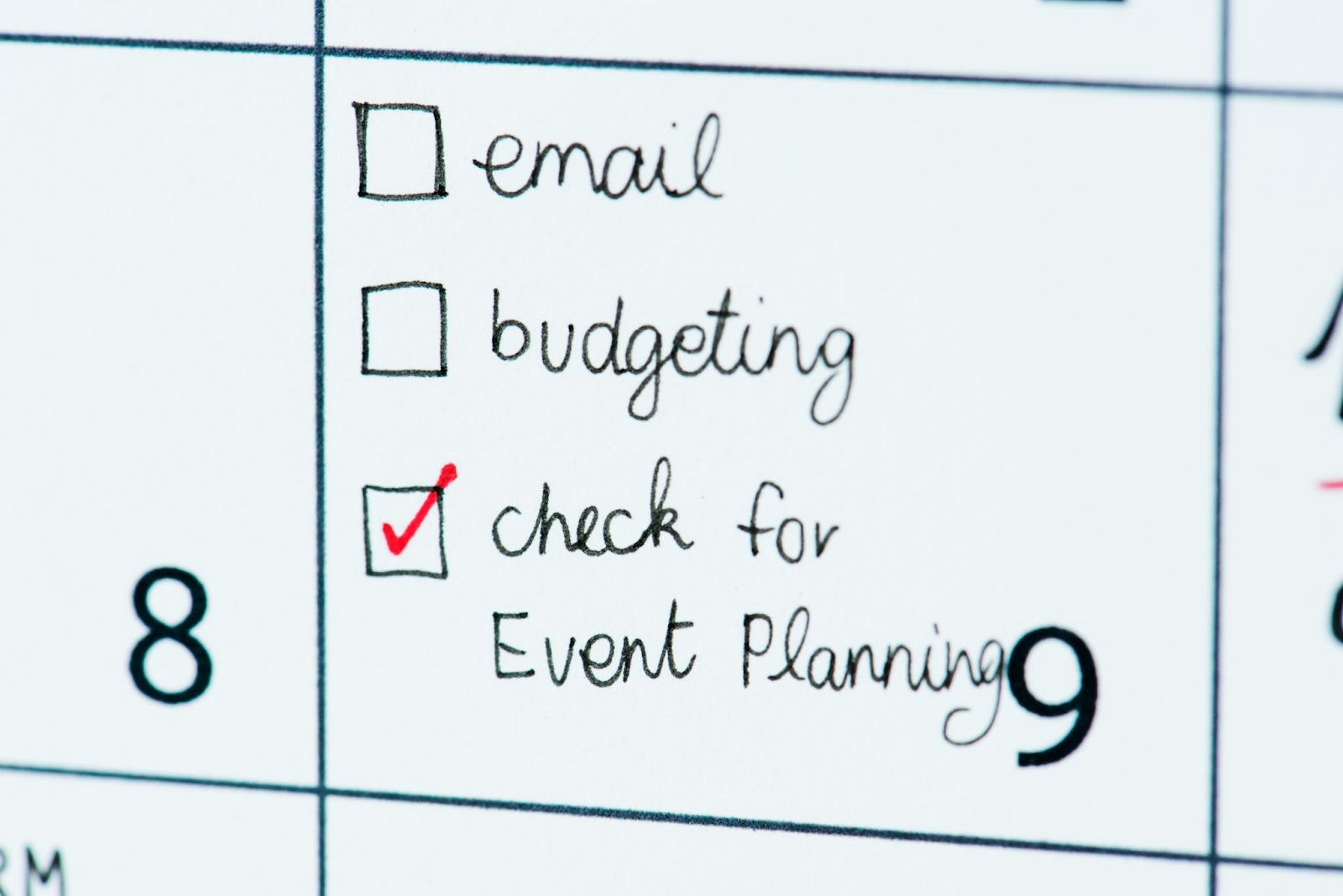 Close-up of a checklist with a red checkmark next to 'check for event planning,' indicating a completed task. The checklist includes other items like 'email' and 'budgeting,' which are yet to be checked off. The focus on the event planning task suggests a prioritized action in the context of organizing an event, set against the backdrop of a planner or calendar.