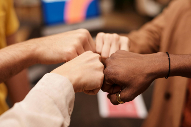 Close-up of a diverse team's hands coming together in a fist bump over a blurred office background, symbolizing teamwork, unity, and collaboration in a multicultural workplace.