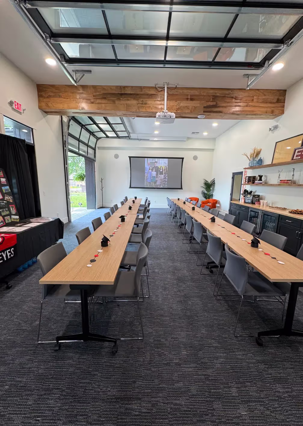 A modern conference room in one of the top event spaces Columbus Ohio offers, featuring two long tables in a U-shape with notepads, pens, a projector screen, and large windows that fill the meeting room with natural light.
