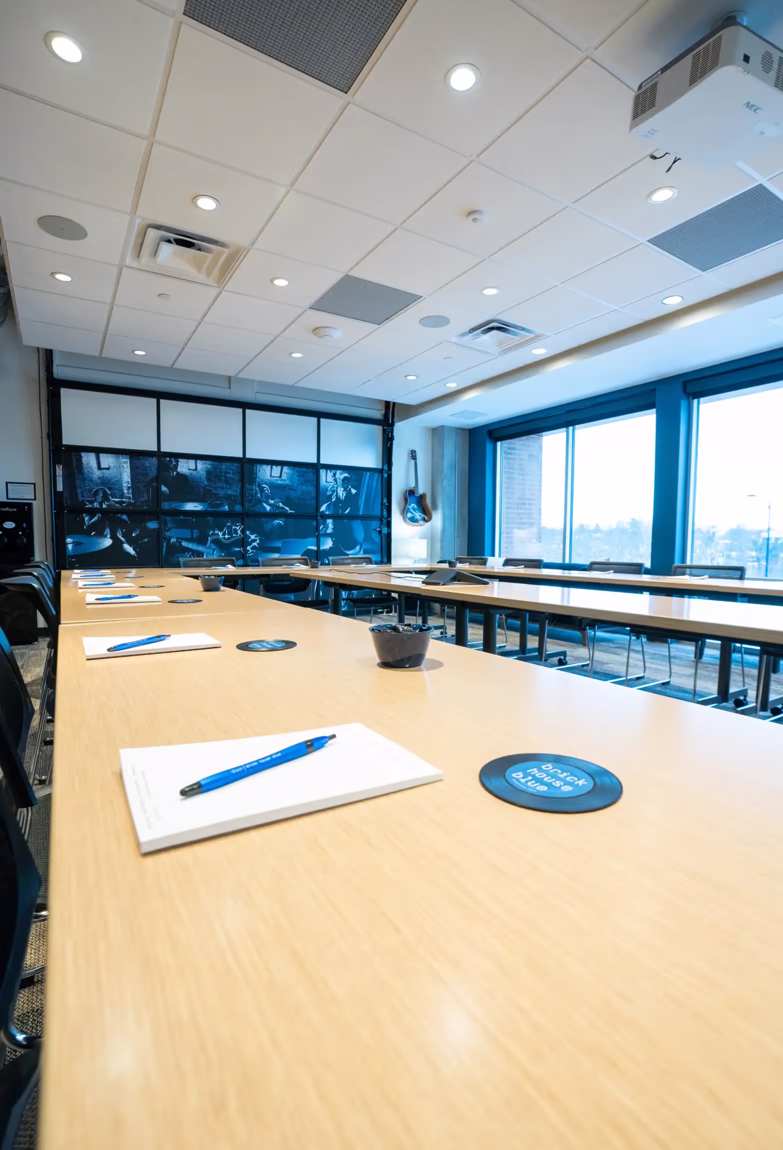 A modern conference room with large windows and U-shaped tables, perfect for meetings or seminars. Each seat has a notepad, blue pen, and coaster. Ideal for those seeking professional meeting rooms or office space for rent.