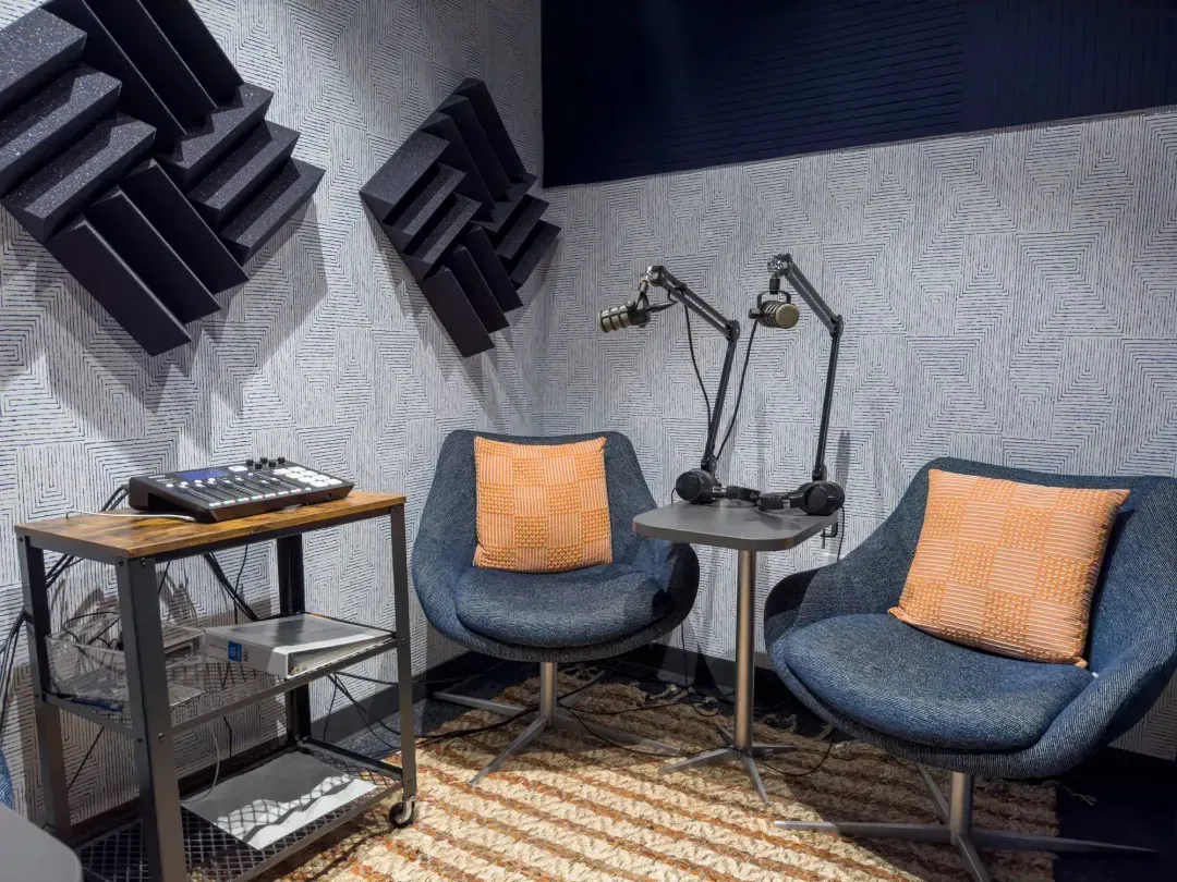 A modern podcast recording studio with two blue chairs, orange cushions, two microphones on stands, soundproofing foam panels, and audio equipment on a metal cart—perfect for content creators or small meeting rooms in Columbus, Ohio.