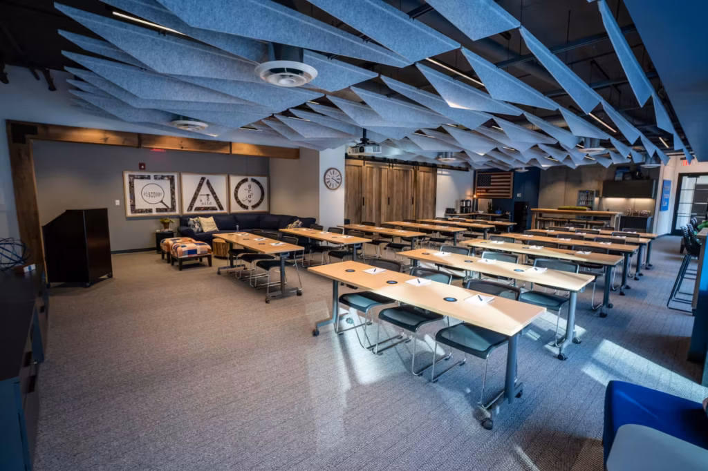 A modern classroom or training room with long desks and chairs arranged in rows, abstract acoustic panels on the ceiling, wood accents, and educational posters on the wall—ideal office space for rent that's spacious, well-lit, and perfect for meetings or workshops.
