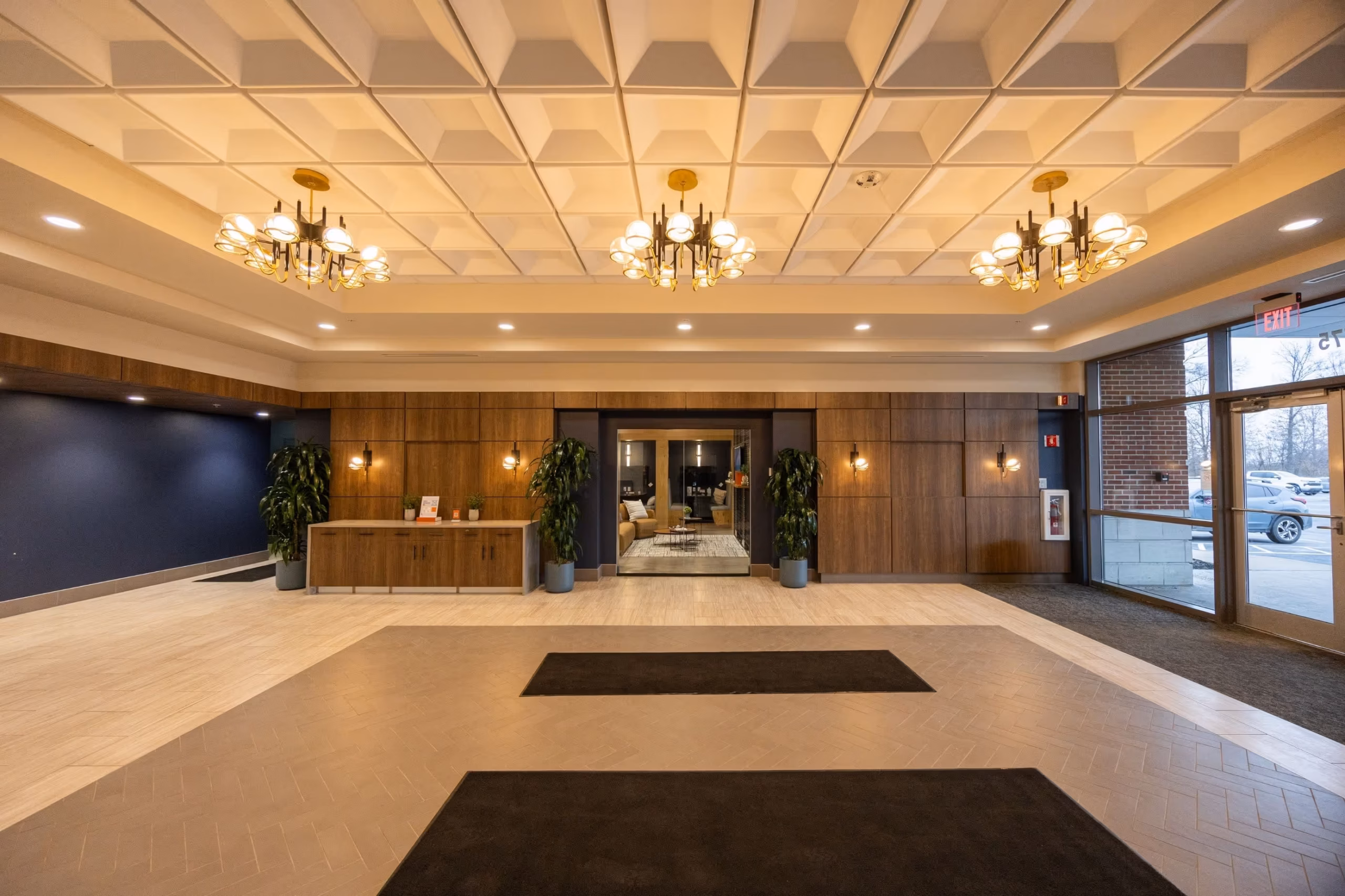 Modern hotel lobby with wood-paneled walls, chandeliers, large plants, and a seating area visible through glass doors. Natural light fills meeting rooms nearby, making it ideal for event spaces Columbus Ohio guests will love.