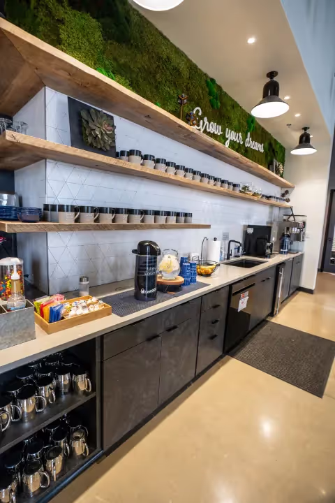 A modern coffee station with mugs, coffee machines, condiments, and shelves lined with jars. Greenery and “Grow your dreams” decor add inspiration—perfect for breaks between meetings in our event spaces Columbus Ohio. Countertop is neat and organized.
