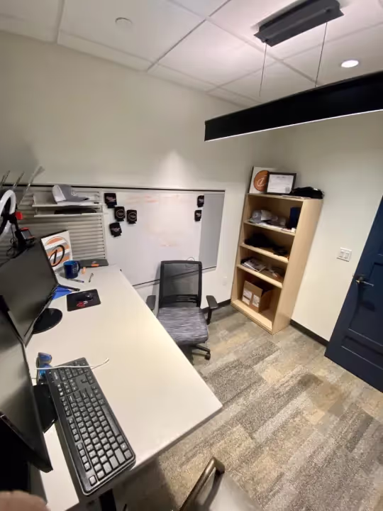 A modern office workspace with a desk, dual monitors, a keyboard, an office chair, a whiteboard with writing, shelves, gray carpeted flooring—ideal for private offices or those seeking flexible office space for rent.