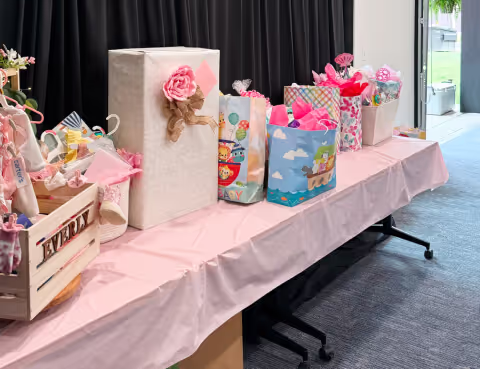 A table covered with a pink tablecloth is decorated with colorful gift bags and boxes, some with ribbons and bows, set up for a celebration or party in one of the stylish event spaces Columbus Ohio offers. A window shows outdoor greenery in the background.